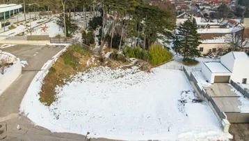 Luftaufnahme eines schneebedeckten Grundstücks mit Bäumen und einem modernen Gebäude im Hintergrund.