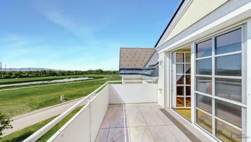 Geräumiger Balkon mit Fliesenboden und weitem Blick über die grüne Landschaft und einen See.