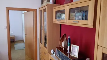 Gemütlicher Wohnbereich mit Holzmöbeln, roter Akzentwand und Zugang zu einem weiteren Zimmer.