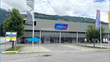 Außenansicht eines modernen Geschäftsgebäudes mit großem Parkplatz und Bergkulisse im Hintergrund.