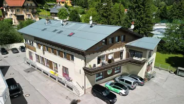 Luftaufnahme des Gebäudes mit umliegender Natur und Parkplätzen unter blauem Himmel.