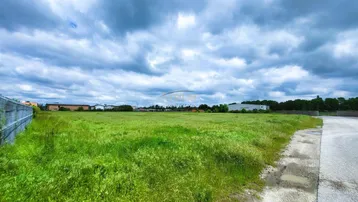Weitläufiges grünes Grundstück unter bewölktem Himmel mit Blick auf entfernte Gebäude.