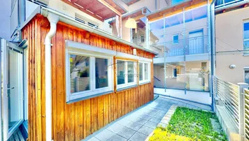 Außenbereich mit Holzverkleidung, gepflastertem Weg und Blick auf die moderne Glasfassade.