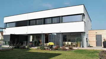 Modernes Einfamilienhaus mit weißer Fassade, großen Fenstern und gepflegtem Gartenbereich.
