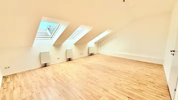 Heller Dachgeschossraum mit Holzboden, weißen Wänden und drei Dachfenstern für viel Tageslicht.