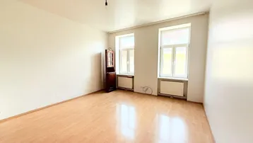 Heller, leerer Raum mit Laminatboden, hohen Decken und zwei großen Fenstern.