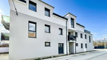 Modernes Neubaugebäude mit weißer und grauer Fassade, großen Fenstern und einem kleinen Balkon.
