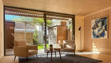 Helles Wohnzimmer mit Holzwänden, großen Schiebetüren und Blick in den Gartenbereich.