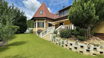 Charmantes Haus mit gelber Fassade, rotem Ziegeldach und gepflegtem Gartenbereich mit Treppe.