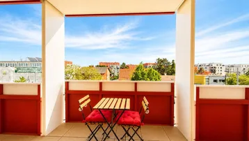 Heller Balkon mit Fliesenboden und rotem Mobiliar, bietet einen weiten Blick über die Umgebung.