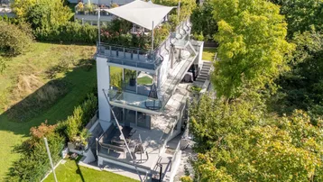 Moderne Architektur mit mehreren Terrassen und Dachterrasse, umgeben von viel Grün.