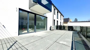 Große, sonnige Terrasse mit Glasgeländer und Zugang zu einem modernen Wohngebäude.