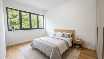 Modernes Schlafzimmer mit Holzboden, großem Fenster und Blick ins Grüne.