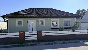 Einfamilienhaus mit hellgrüner Fassade, Satteldach und weißem Zaun im Vorgarten.