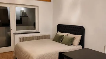 Modernes Schlafzimmer mit Doppelbett, kleinem Tisch und stilvoller Deckenleuchte.