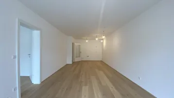 Geräumiges, leeres Wohnzimmer mit hellem Parkettboden und weißen Wänden, bereit zur Einrichtung.