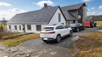 Ländliches Anwesen mit Wohnhaus, Scheune und Fahrzeugen unter blauem Himmel.