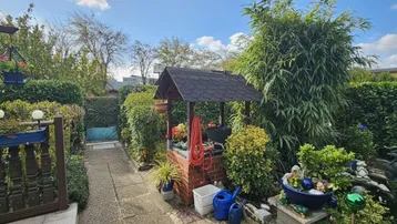 Gepflegter Gartenbereich mit dekorativem Brunnen, üppiger Bepflanzung und einem gepflasterten Weg.
