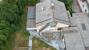 Luftaufnahme eines Einfamilienhauses mit Garten, Weg und angrenzenden Grundstücken in grüner Umgebung.