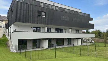Modernes Mehrfamilienhaus mit klarer Architektur, Balkonen, Terrassen und gepflegter Rasenfläche in grüner Umgebung.