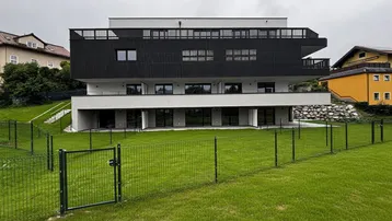 Moderne Wohnanlage mit schwarzer Lamellenfassade und weißem Sockelgeschoss, umgeben von einer Grünfläche.