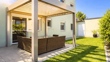 Moderne Terrasse mit Pergola und bequemen Loungemöbeln, umgeben von einem gepflegten Rasen.