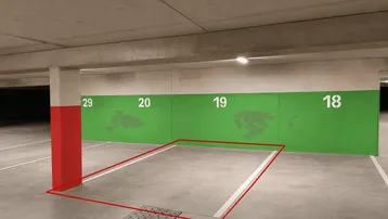 Markierter Tiefgaragenstellplatz mit roter Säule und grüner Wand in einer modernen Parkgarage.