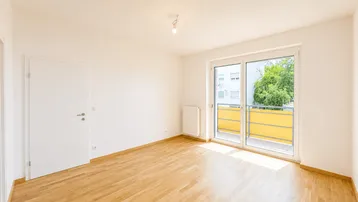 Helles, leeres Zimmer mit Parkettboden und Zugang zu einem Balkon, ideal als Wohnzimmer nutzbar.