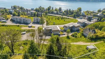 Luftaufnahme eines Grundstücks mit Seeblick und umliegender Bebauung in grüner Landschaft.