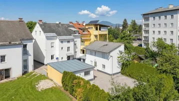 Vogelperspektive einer Wohnsiedlung mit verschiedenen Gebäuden, Grünflächen und Bergen im Hintergrund.