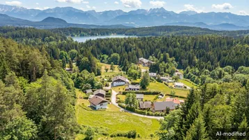 Malerische Luftaufnahme eines Dorfes umgeben von Wäldern, mit einem See und Bergen im Hintergrund.