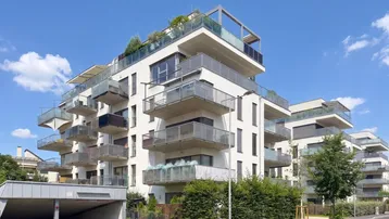 Modernes Mehrfamilienhaus mit vielen Balkonen und Tiefgaragenzufahrt unter blauem Himmel.