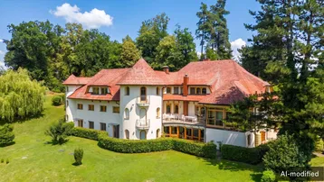 Große Villa mit rotem Ziegeldach, umgeben von üppigem Grün und altem Baumbestand.
