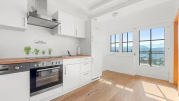 Moderne weiße Küche mit Holzarbeitsplatte, Einbaugeräten und Zugang zu einem Balkon mit Weitblick.