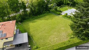 Luftaufnahme eines großen, grünen Baugrundstücks neben einem Haus mit Carport und Solaranlage.