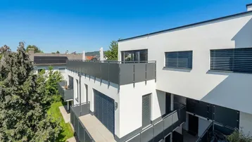 Moderne Wohnanlage mit mehreren Balkonen und Terrassen, umgeben von Grünflächen unter blauem Himmel.