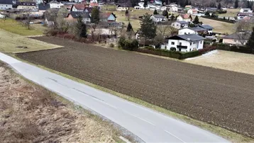Luftaufnahme eines unbebauten Grundstücks neben einer Straße mit Häusern im Hintergrund und ländlicher Umgebung.