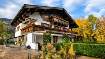 Traditionelles Haus im alpinen Stil mit Holzbalkonen, Wintergarten und gepflegtem Gartenbereich.