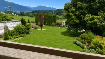 Gepflegter Garten mit weitem Blick auf die umliegende Berglandschaft und grüne Felder.