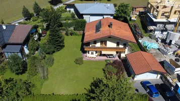 Luftaufnahme eines traditionellen Hauses mit großem Garten, Balkon und angrenzender Garage in ländlicher Umgebung.