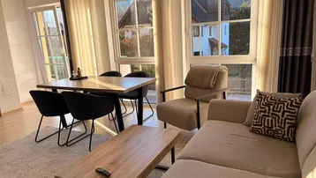 Helles Wohn- und Esszimmer mit großen Fenstern, Parkettboden und Blick ins Grüne.
