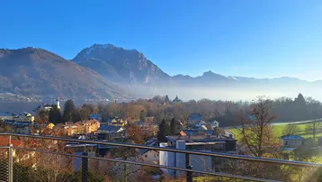 Panoramablick vom Balkon auf den See, die Stadt und die umliegenden Berge an einem sonnigen Tag.