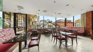 Geräumiger Gastronomiebereich mit großen Fenstern, die einen Blick auf die umliegenden Gebäude bieten.