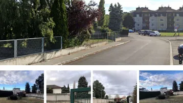 Blick auf die Straße und umliegende Wohngebäude mit einem eingezäunten Grundstück im Vordergrund.