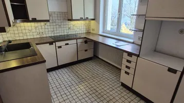 Funktionale Küche mit weißen Fliesen, Einbauschränken und einem Fenster.