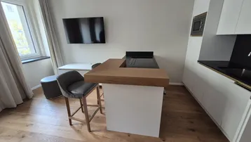 Moderner Wohnbereich mit integrierter Küchenzeile, Holzboden und einem Flachbildfernseher an der Wand.