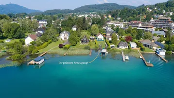 Luftaufnahme von Häusern am Seeufer mit privaten Stegen und üppiger Vegetation.