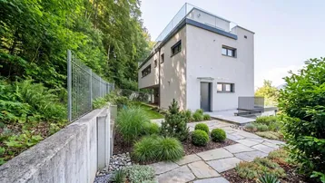 Modernes Haus mit gepflegtem Gartenbereich und Steinfliesenweg, umgeben von viel Grün.