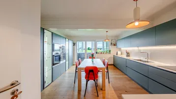 Moderne Küche mit Essbereich, Holzboden und Blick ins Grüne durch große Fenster.
