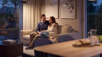 Gemütliches Wohnzimmer mit Sofa, Stehlampe und Blick ins Grüne am Abend.